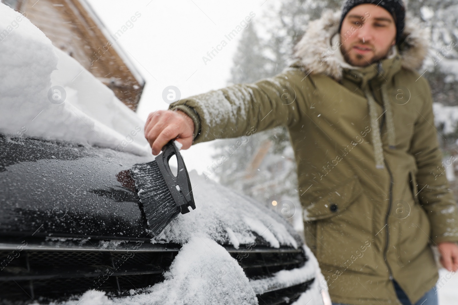 Photo of Young man cleaning snow from car outdoors on winter day