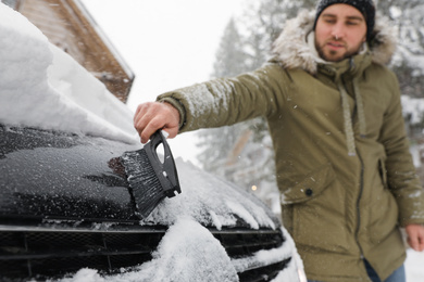 Young man cleaning snow from car outdoors on winter day