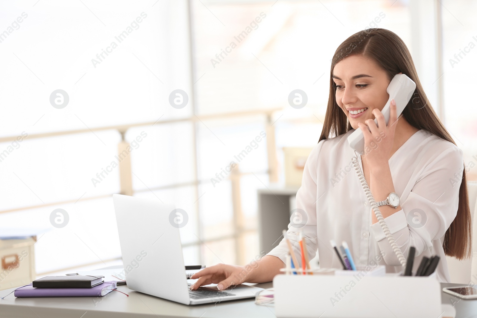 Photo of Young woman talking on phone at workplace