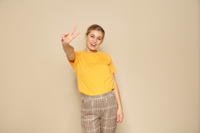 Photo of Happy young woman showing victory gesture on color background