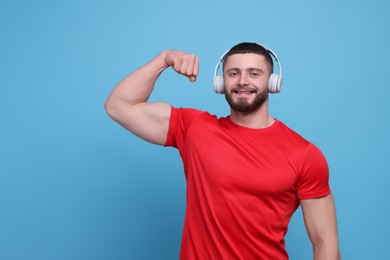 Photo of Handsome man with headphones showing muscles on light blue background, space for text