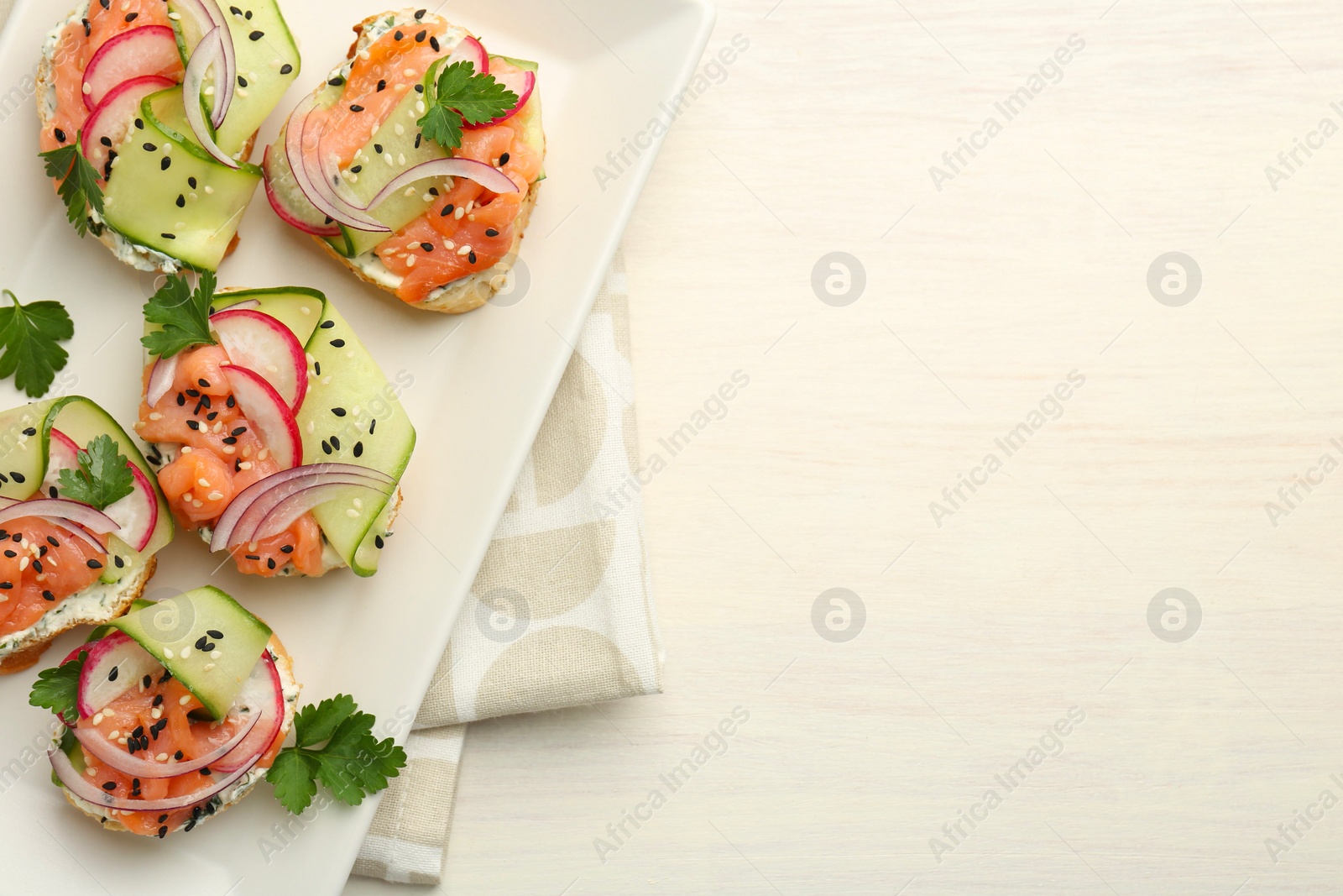 Photo of Tasty canapes with salmon served on white wooden table, top view. Space for text