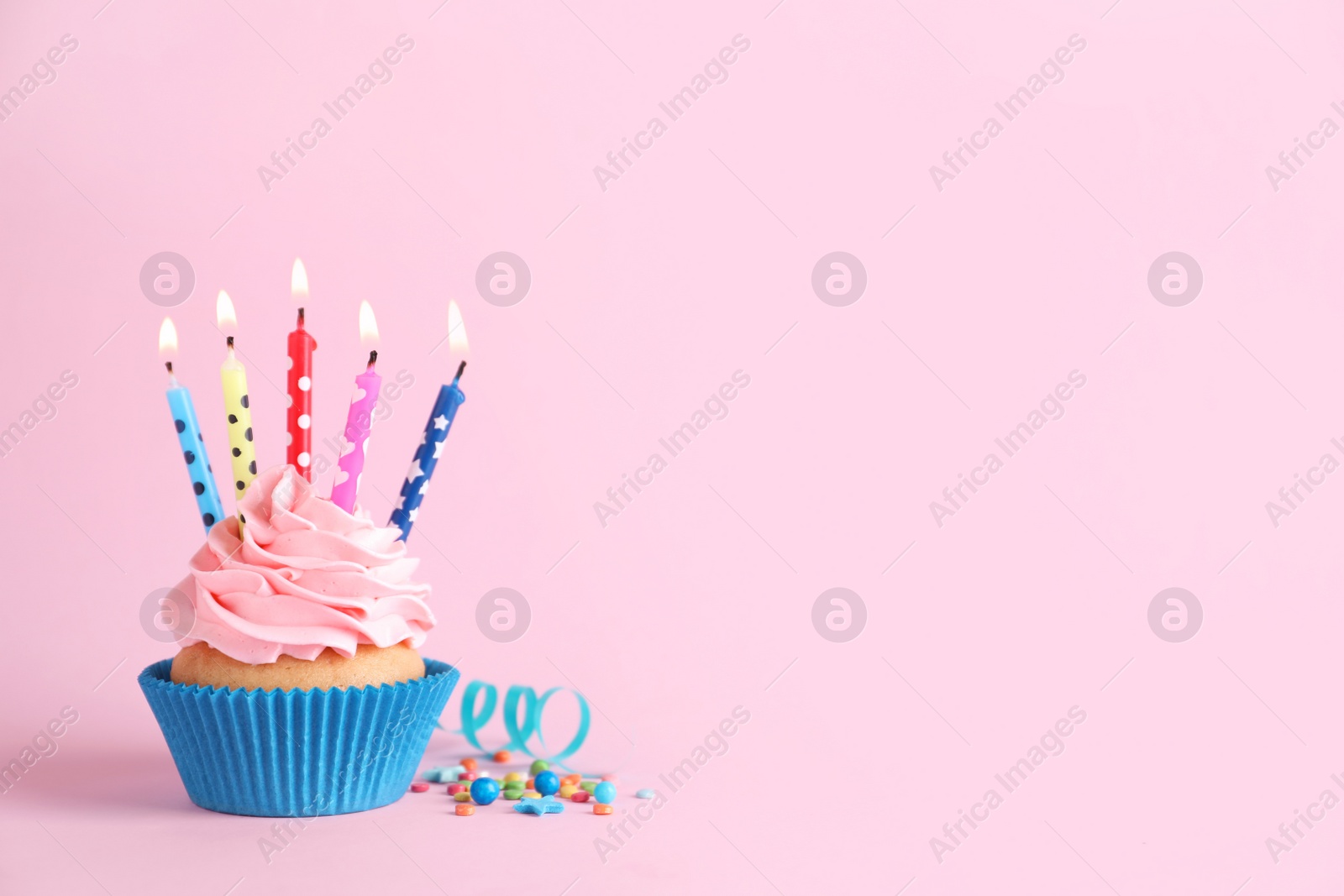 Photo of Delicious birthday cupcake with burning candles, sprinkles and streamer on pink background, space for text