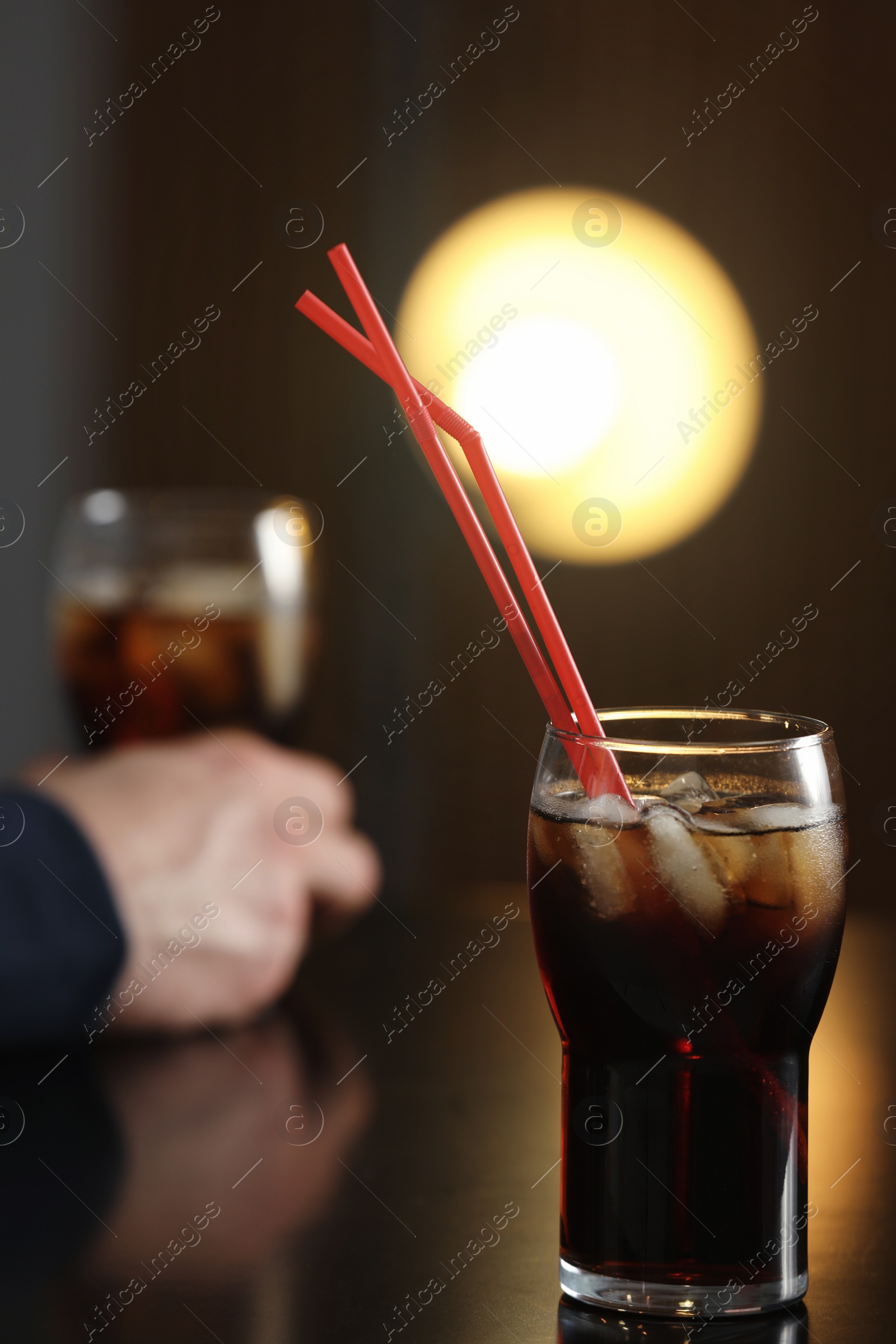 Photo of Glass of cola with ice on table against blurred background