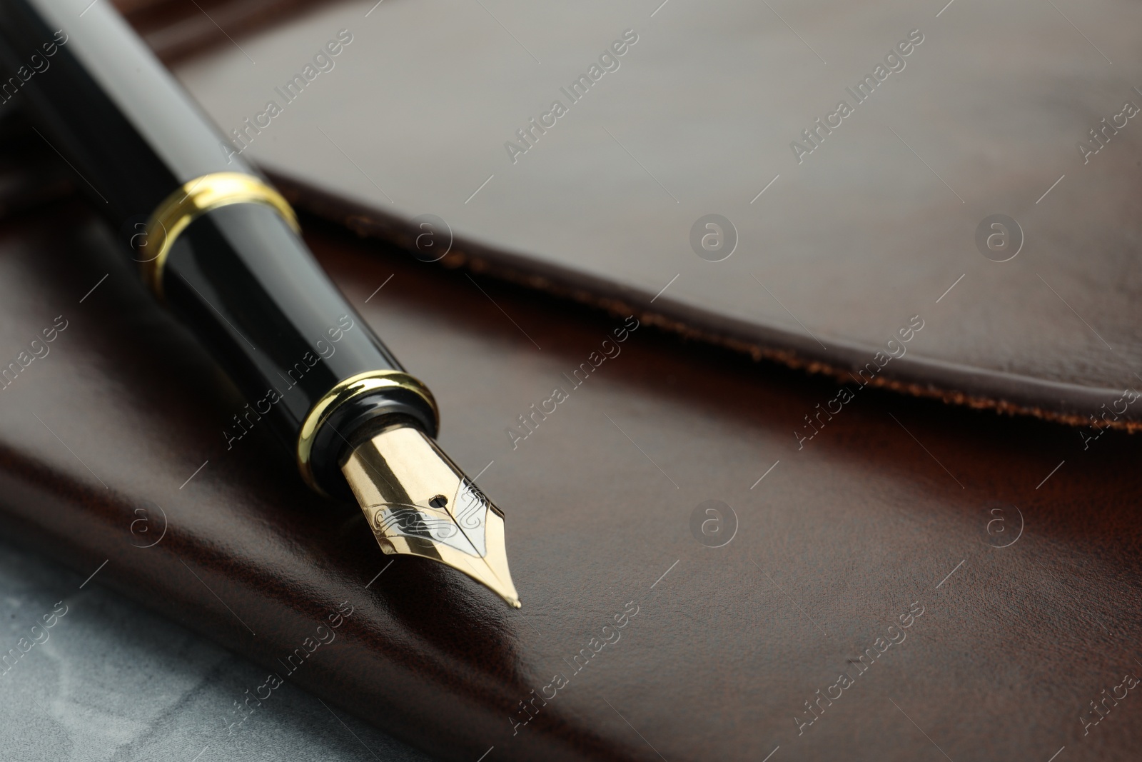 Photo of Stylish fountain pen and leather notebook on light grey table, closeup. Space for text