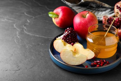 Photo of Honey, pomegranate and apples on black table, space for text. Rosh Hashana holiday