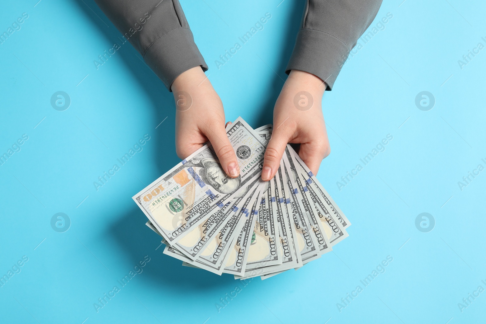 Photo of Money exchange. Woman holding dollar banknotes on light blue background, top view