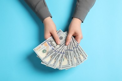 Money exchange. Woman holding dollar banknotes on light blue background, top view