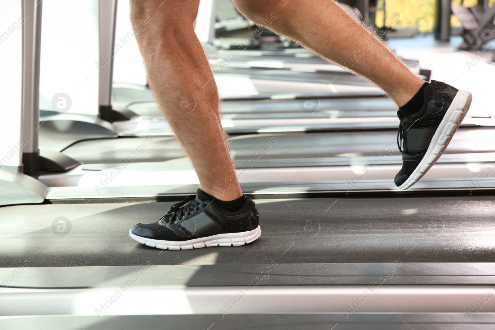 Photo of Strong young man on treadmill in gym, closeup of legs