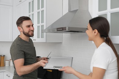 Woman giving filter of cooker hood to man in kitchen