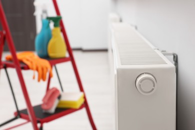 Photo of Modern radiator and ladder with cleaning supplies in room, closeup