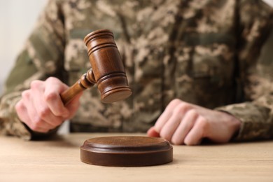 Photo of Law concept. Man in military uniform with gavel at wooden table, closeup