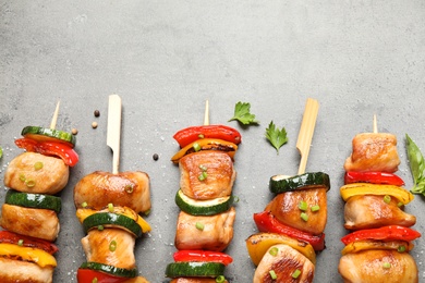 Photo of Delicious chicken shish kebabs with vegetables and herbs on grey table, flat lay. Space for text