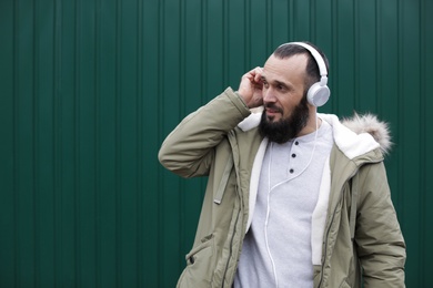 Mature man with headphones listening to music near color wall. Space for text