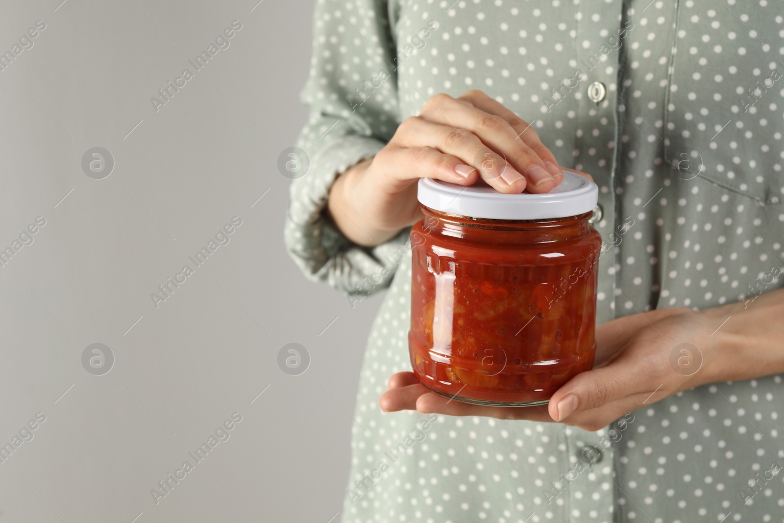 Photo of Woman holding jar of canned lecho on light background, closeup. Space for text