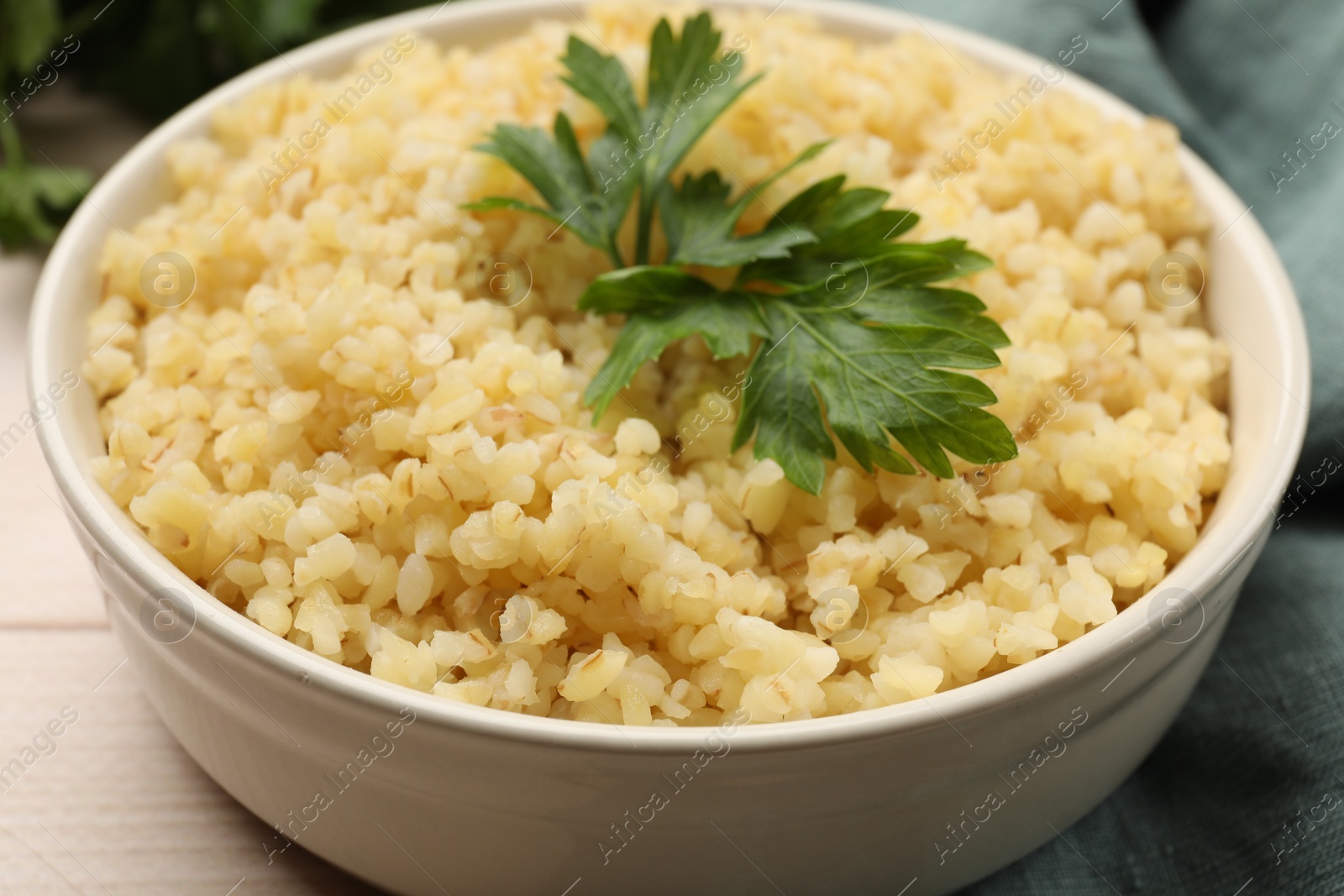 Photo of Delicious bulgur with parsley in bowl on table, closeup