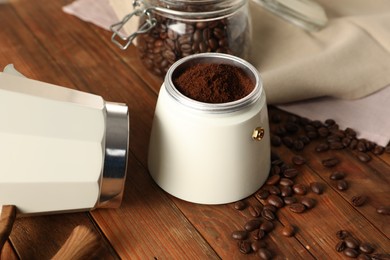 Photo of Moka pot with ground coffee and beans on wooden table