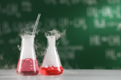 Photo of Laboratory flasks with colorful liquids on white table, space for text. Chemical reaction
