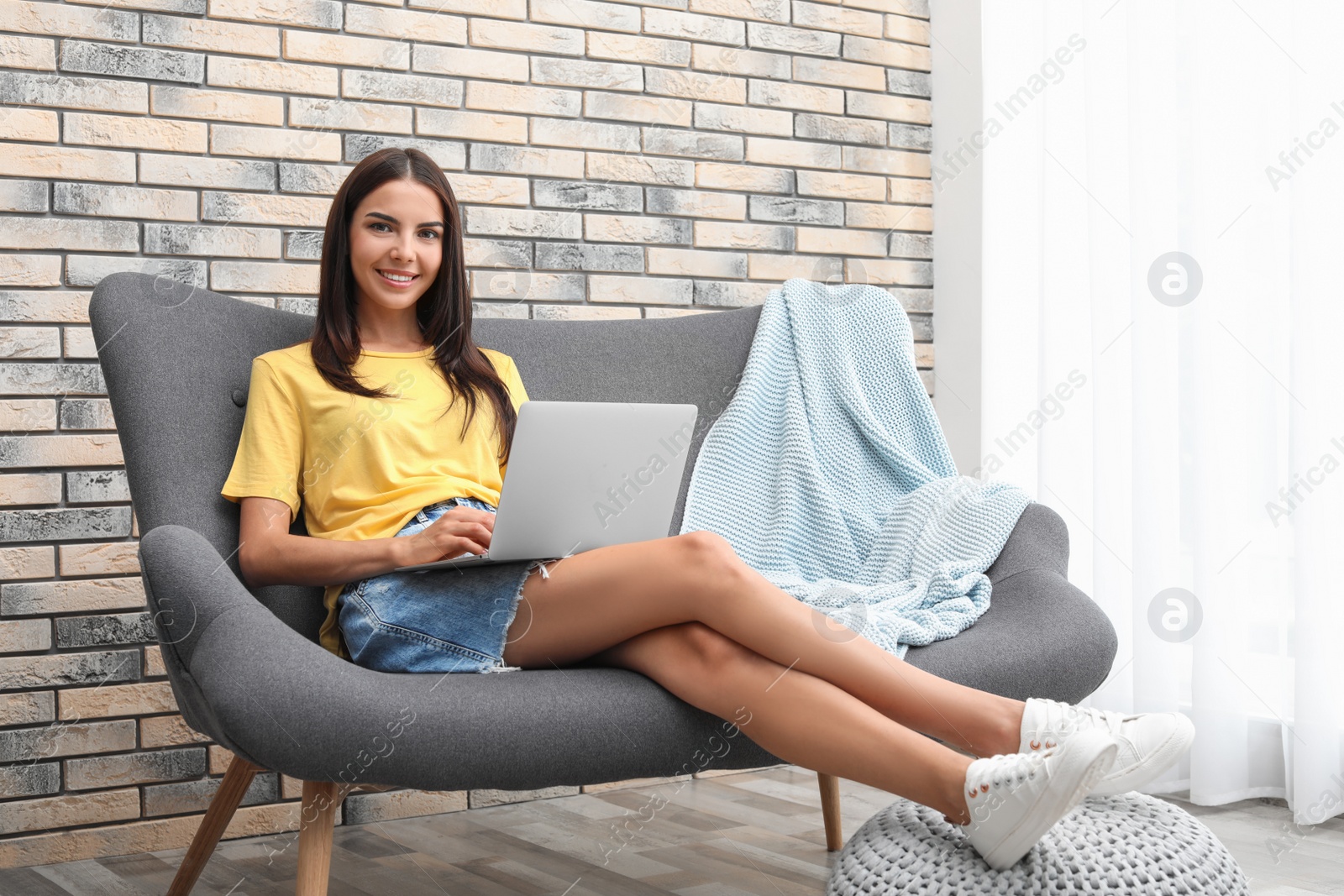 Photo of Young woman with modern laptop sitting on sofa at home