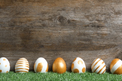 Photo of Line of traditional Easter eggs decorated with golden paint on green lawn near wooden wall, space for text