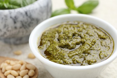 Photo of Tasty pesto sauce in bowl and pine nuts on table, closeup