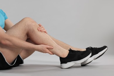 Photo of Man suffering from leg pain on grey background, closeup