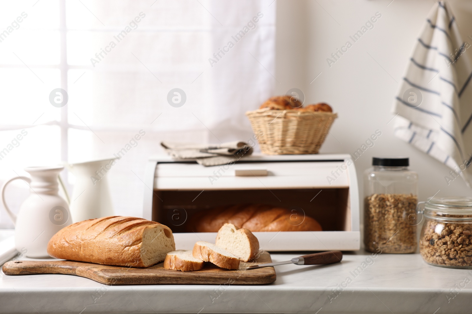 Photo of Wooden bread basket with freshly baked loaves on white marble table in kitchen