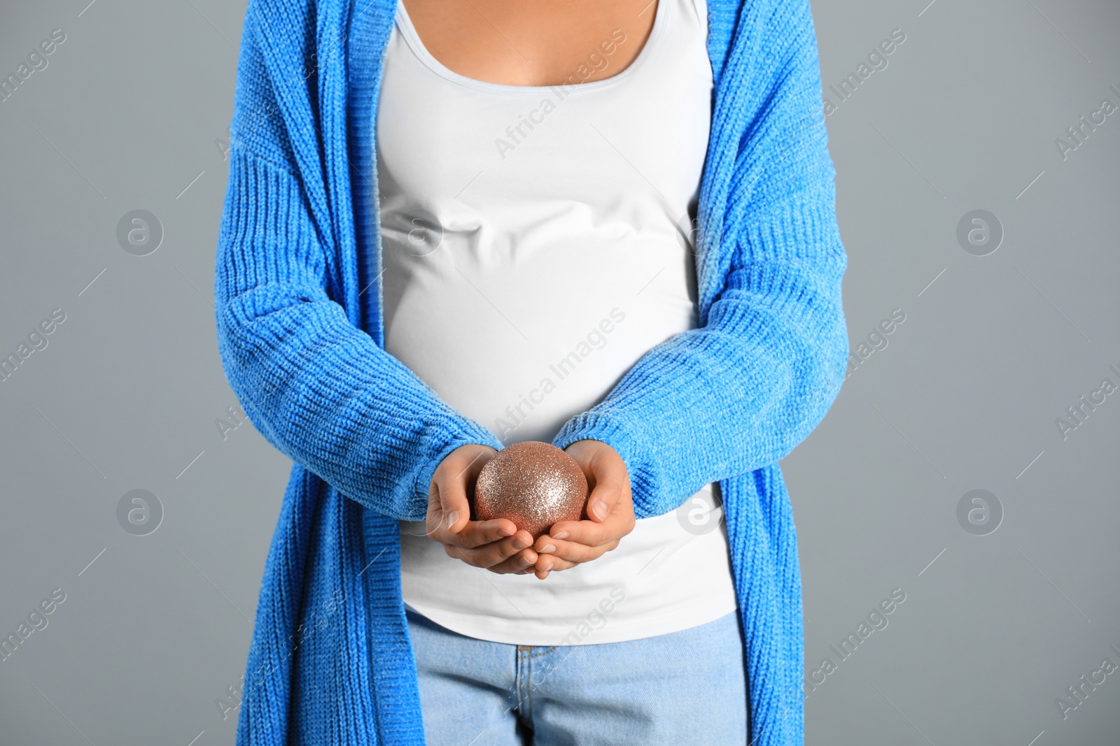 Photo of Pregnant woman with Christmas ball on grey background, closeup. Expecting baby