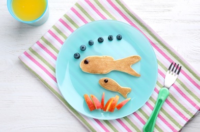 Photo of Tasty pancakes served with blueberries, apple slices and juice on white wooden table, flat lay. Creative idea for kids breakfast