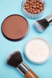 Different face powders and brushes on light blue background, flat lay