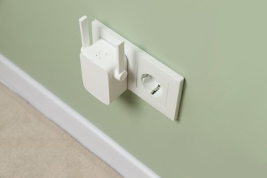 Photo of Wireless Wi-Fi repeater on light green wall indoors, above view