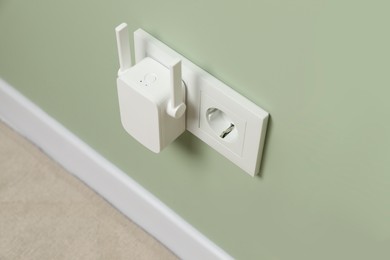 Wireless Wi-Fi repeater on light green wall indoors, above view