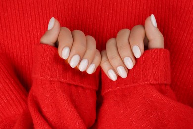 Photo of Woman with white polish on nails on red knitted background, top view