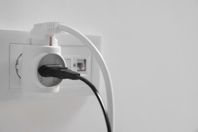 Different electrical power plugs in socket on light wall, closeup. Space for text