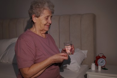 Photo of Elderly woman suffering from insomnia taking pill on bed at night