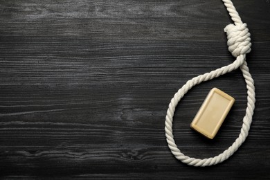 Photo of Rope noose and soap bar on dark wooden table, flat lay. Space for text