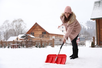 Young woman cleaning snow with shovel near her house. Space for text