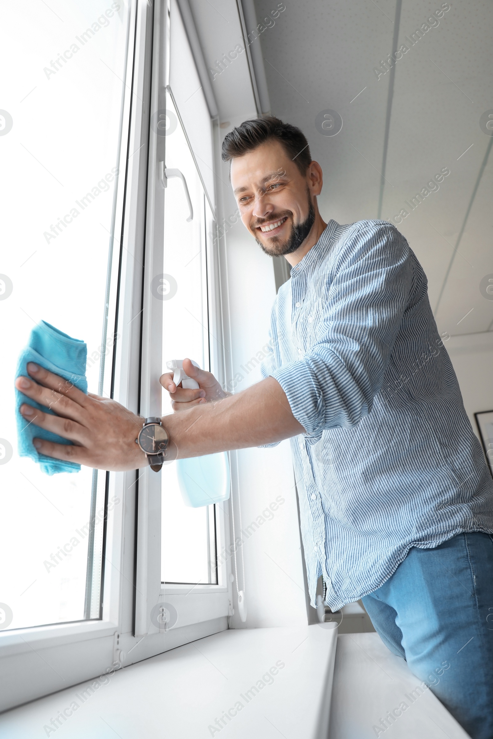 Photo of Man in casual clothes washing window glass at home