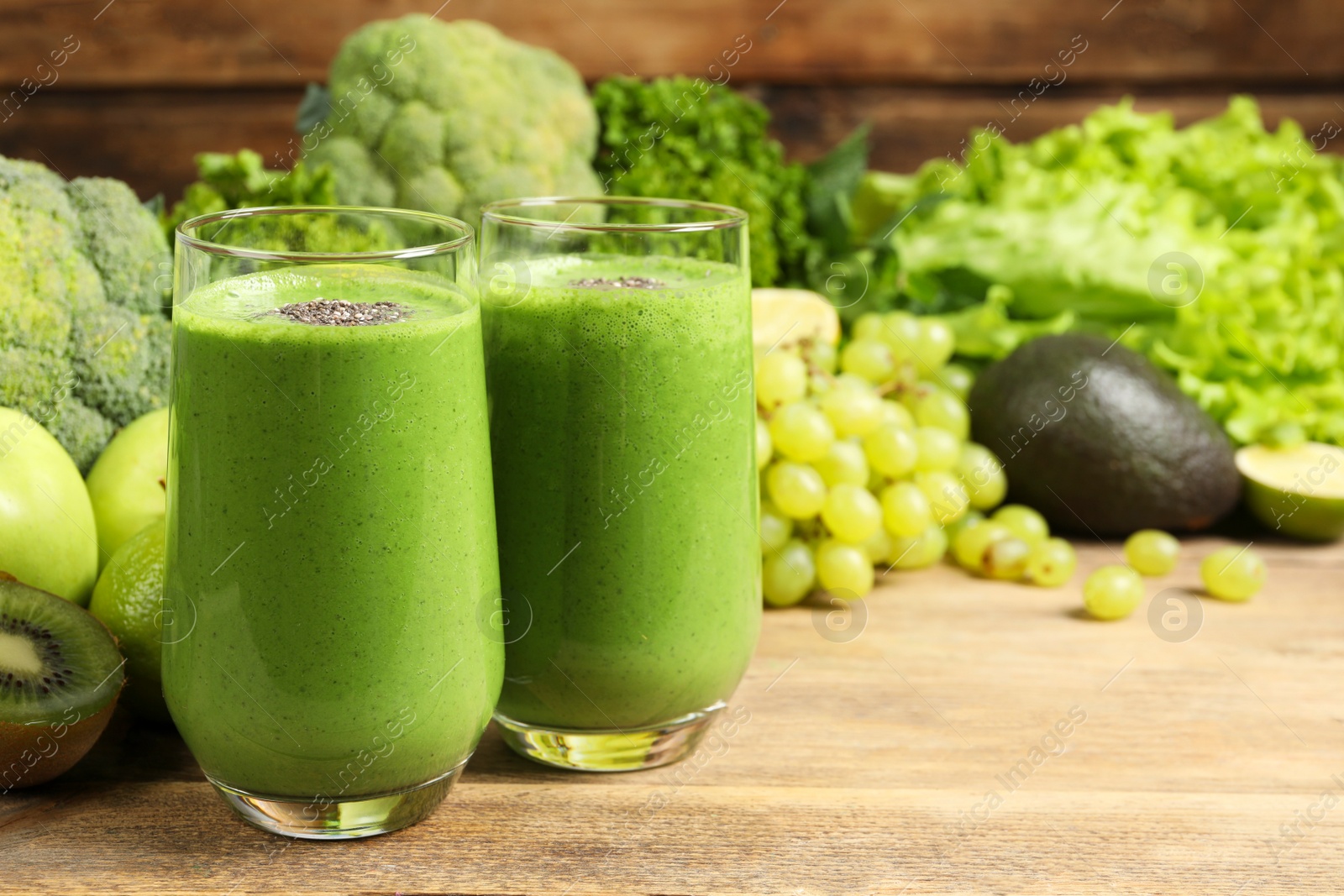 Photo of Glasses of fresh green smoothie and ingredients on wooden table, space for text