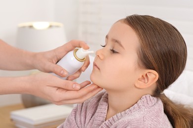 Mother using nasal spray to treat her little daughter indoors, closeup