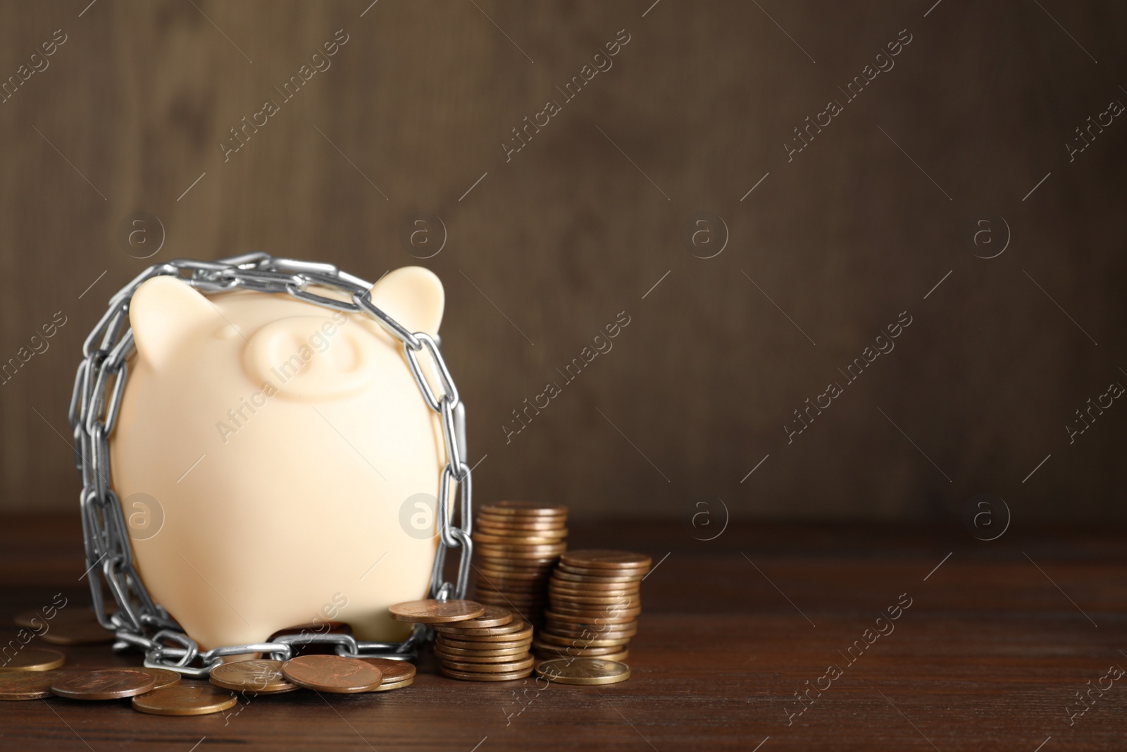 Photo of Piggy bank with steel chain and coins on wooden table, space for text. Money safety concept