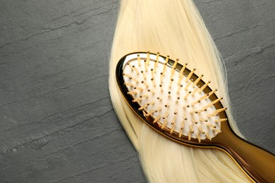 Photo of Stylish brush with blonde hair strand on dark grey table, top view. Space for text