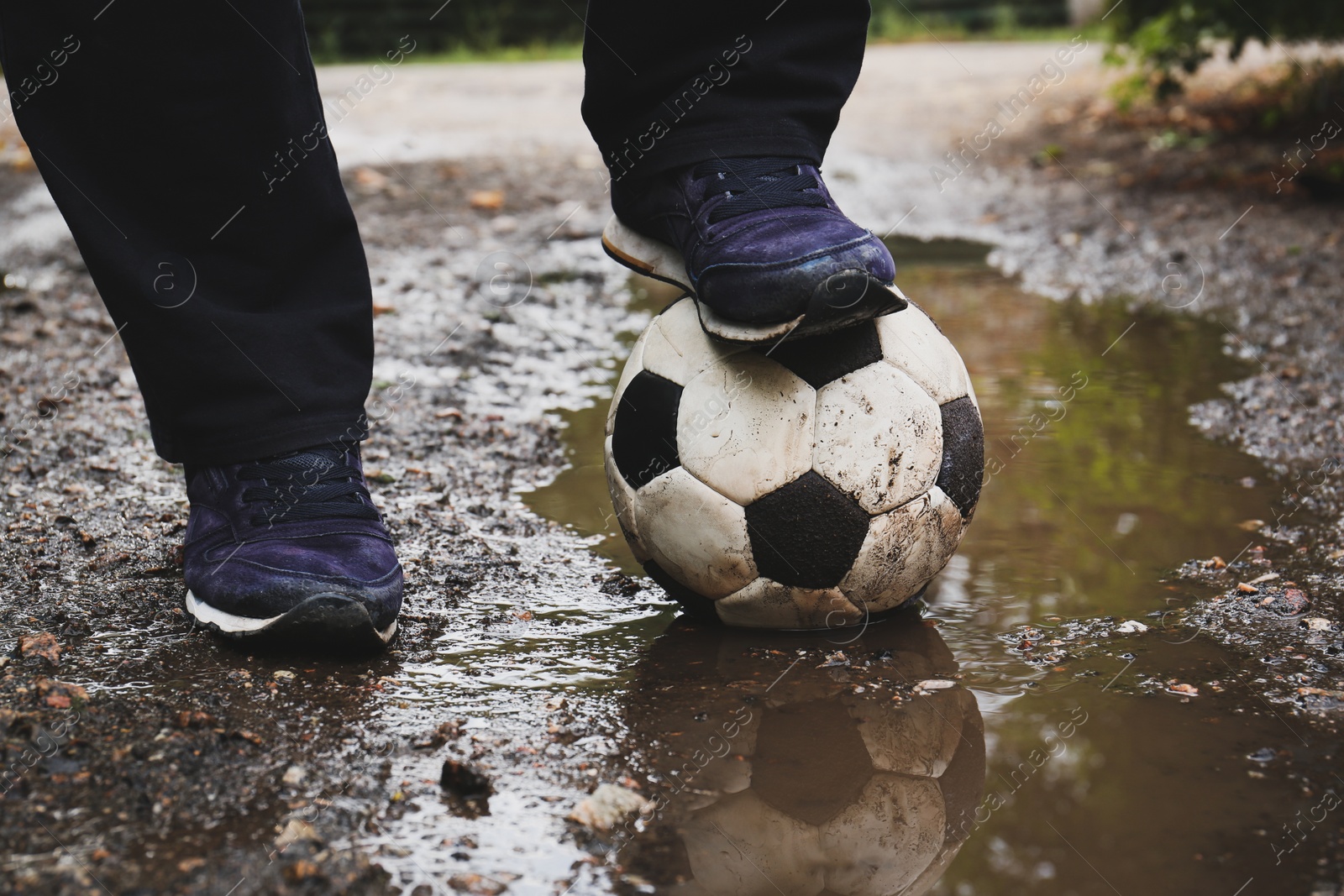 Photo of Man with soccer ball in muddy puddle outdoors, closeup