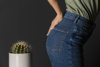 Woman sitting down on cactus against black background, closeup. Hemorrhoid concept
