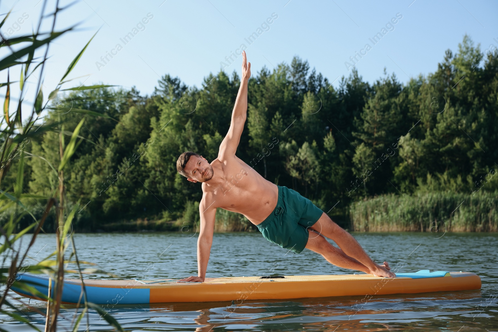 Photo of Man practicing yoga on color SUP board on river