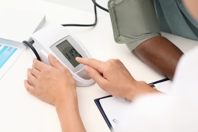 Photo of Young doctor checking African-American patient's blood pressure in hospital