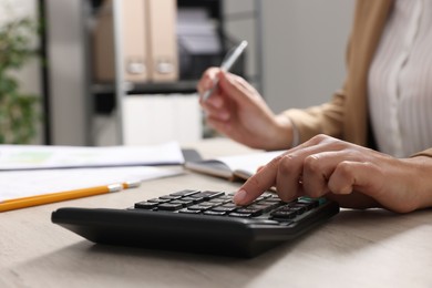 Photo of Woman using calculator while taking notes at wooden table indoors, closeup