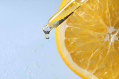 Photo of Dripping cosmetic serum from pipette onto orange slice against light blue background, top view. Space for text