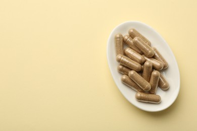 Photo of Vitamin capsules on pale yellow background, top view. Space for text