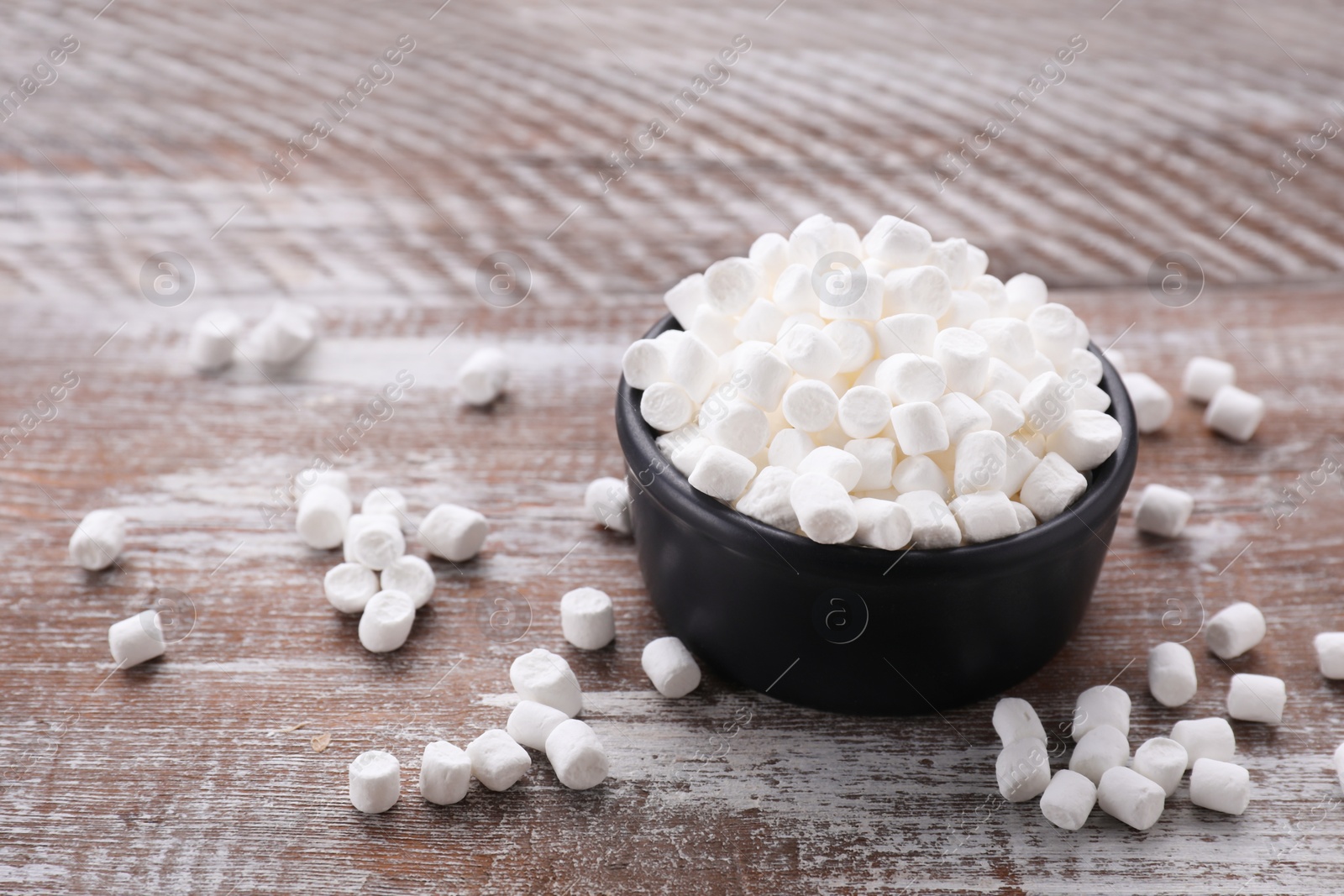 Photo of Bowl with delicious marshmallows on wooden table